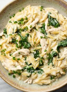 a bowl filled with pasta and spinach on top of a marble countertop next to a fork