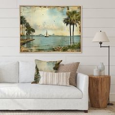 a living room with a white couch and painting on the wall above it that has palm trees