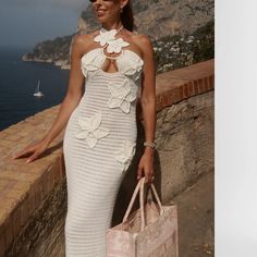 a woman in a white dress holding a pink bag and standing next to the ocean