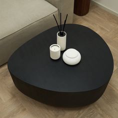 a black table with two white vases and candles on it in front of a couch