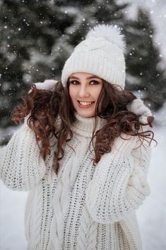 a woman wearing a white hat and sweater in the snow with her hands on her hair