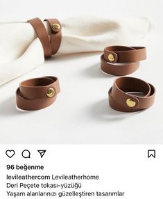 three brown leather bracelets sitting on top of a white cloth next to a napkin