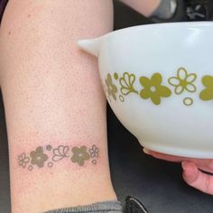 a woman holding a white bowl with flowers on it and a small tattoo on her arm