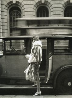 a woman standing in front of a car on the street with her handbag and purse