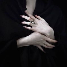 a woman with her hands on her chest wearing a black hoodie and white ring