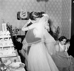 a bride and groom are kissing in front of their wedding cake while others look on