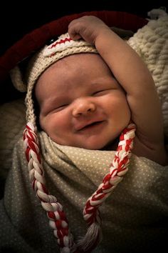 a smiling baby wrapped in a blanket and wearing a knitted hat with candy canes on it's head