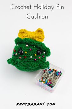 a crochet holiday pin cushion next to a container with pins and needles in it