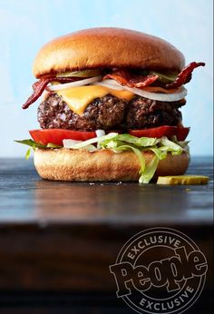 a cheeseburger with bacon, lettuce and tomato on a wooden table