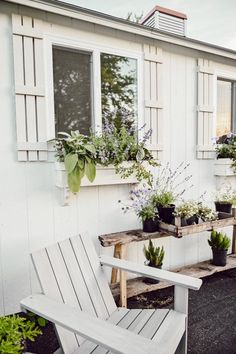 a wooden bench sitting in front of a white building with potted plants on it