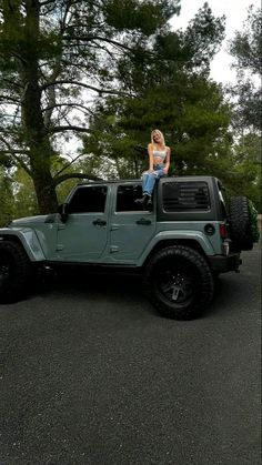 a woman sitting on top of a green jeep