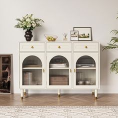 a white cabinet with glass doors and gold handles in front of a potted plant