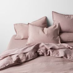 an unmade bed with pink linens and pillows on the bottom, in front of a white wall