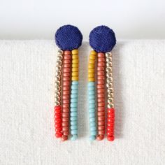 two pairs of colorful beaded earrings on top of a white cloth covered tablecloth