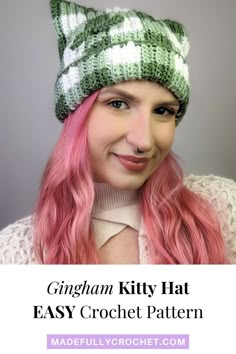 a woman with pink hair wearing a green and white knitted kitty hat, smiling at the camera