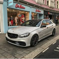 a silver car parked in front of a store on the side of a street with people walking by