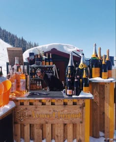 an outdoor bar with bottles of wine on it and snow covered mountains in the background