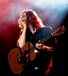 a woman with long hair holding a guitar and singing into a microphone while standing on stage