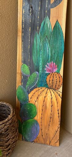 a wooden sign painted with cactus and succulents next to a wicker basket