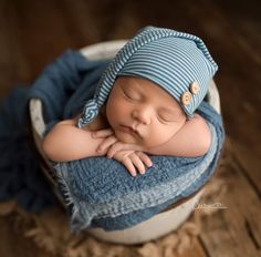 a newborn baby is sleeping in a bowl wearing a blue hat and striped shirt with buttons