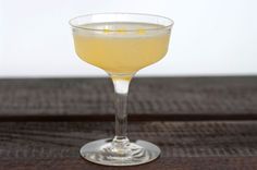 a glass filled with yellow liquid sitting on top of a wooden table