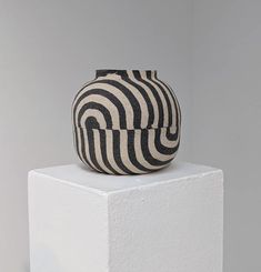 a black and white striped vase sitting on top of a block in front of a gray wall