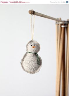 a small white snowman ornament hanging from a wooden pole in front of a white wall