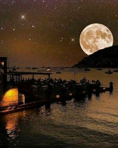 the full moon is shining brightly in the night sky over boats docked on the water