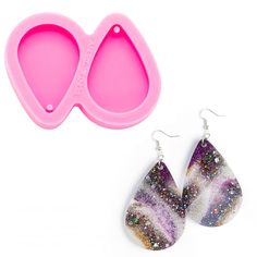 two pairs of earrings with pink and purple designs on them next to a plastic spoon