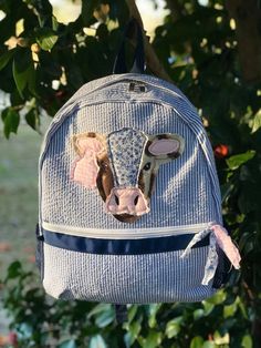 a blue backpack with a cow head on it hanging from a tree branch in front of some leaves