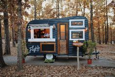 a small blue and white trailer parked in the woods next to some trees with leaves on it