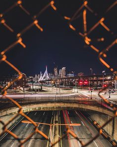 the city skyline is seen through a chain link fence in this view from an overpass