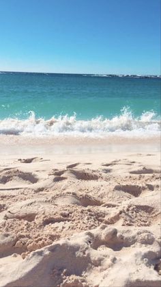 a surfboard sitting on top of a sandy beach next to the ocean with waves coming in