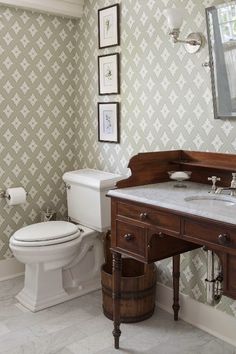 a white toilet sitting next to a wooden sink vanity in a bathroom under a mirror