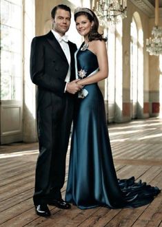 a man and woman in formal wear posing for a photo on a wooden floor with chandeliers