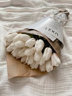 a bunch of white tulips are wrapped in brown paper on a bed sheet