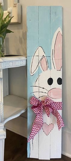 a wooden sign with a bunny painted on it's face and a bow around its neck