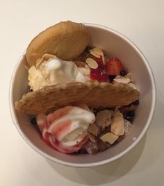 a bowl filled with ice cream and fruit on top of a white table next to a spoon