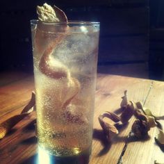 a glass filled with liquid sitting on top of a wooden table next to an orange peel