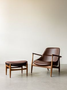 a chair and foot stool sitting in front of a white wall with a brown leather ottoman