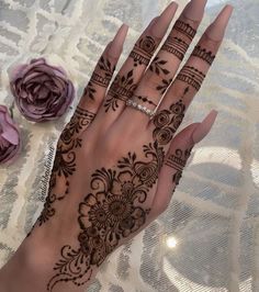 a woman's hand with henna tattoos on it and flowers in the background