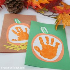 two paper bags with handprints on them next to autumn leaves and pine cones