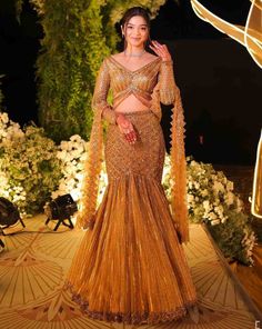 Antique gold fishcut lehenga with all over sequin, crystal and cutdana embroidery. Paired with a striking full sleeves V neck blouse with hanging tassel detailing and embroidered dupatta in net.From Isa by Dolly Wahal's Farra collection.DELIVERY TIMEPlease allow 8-12 weeks for your outfit to arrive.FABRIC DETAILSNetProfessional cleaning only. Gold Embellished Gown For Festivals, Flare Lehenga, Cutdana Embroidery, Hand Embroidered Blouse, Embroidered Dupatta, Dark Gold, 12 Weeks, V Neck Blouse, Full Sleeves