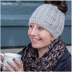 a woman is holding a coffee cup and wearing a knitted hat with her hair in a bun