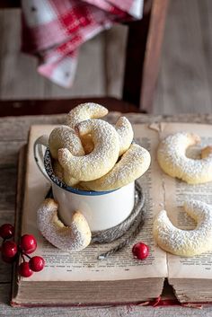 some powdered sugar donuts are in a white cup on top of an open book