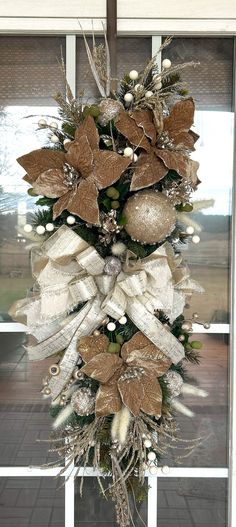 a christmas wreath hanging from the side of a window with white and gold decorations on it