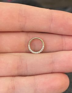 a person's hand holding a gold ring with small white stones on the inside