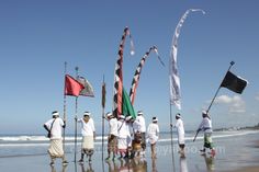 several people are standing on the beach with flags and poles in front of them,