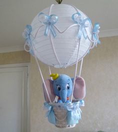 an elephant in a basket hanging from the ceiling with a blue bow on it's head