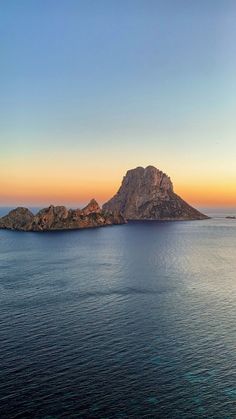 an island in the middle of the ocean at sunset, with one large rock sticking out of the water